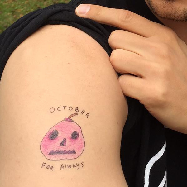Person’s arm with a tattoo of pink/red hand-drawn jack-o-lantern with handwritten text that says “October For Always”.