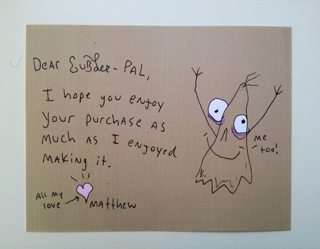Brown notecard with handwritten lettering that says “Dear Gubler-Pal, I hope you enjoy your purchase as much as I enjoyed making it. All my love, arrow to heart drawing. Matthew. Hand-drawn ghost on right side with arms up saying “Me too”.
