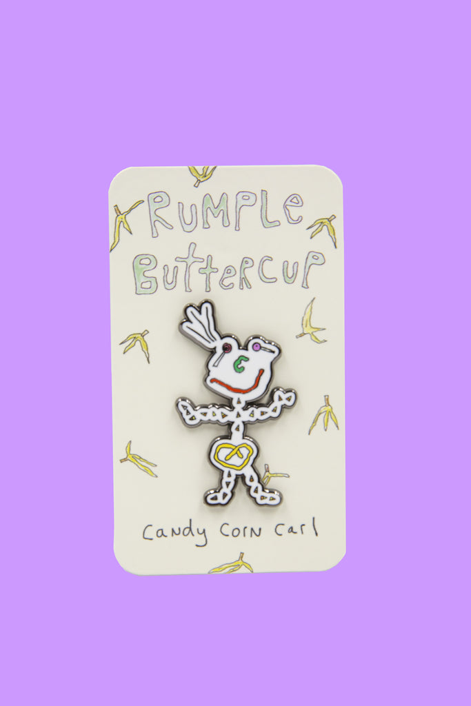 Enamel pin of Candy Corn Carl in front of paper card covered in hand-drawn bananas.