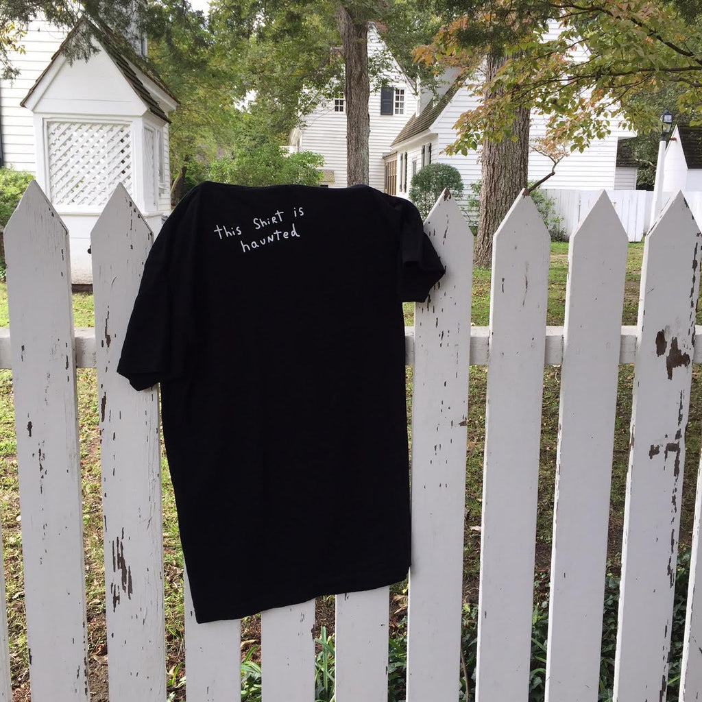 T-shirt hanging on picket fence with the handwriting on it that says “this shirt is haunted”