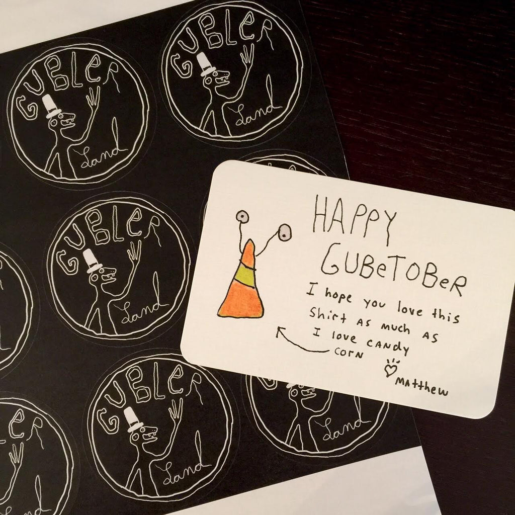 Hand drawn candy corn with eyeballs on a card with handwriting that says “ Happy October I hope you love this shirt as much as I love candy corn- Matthew”. Card is sitting on top of a sheet of Gublerland logo stickers.