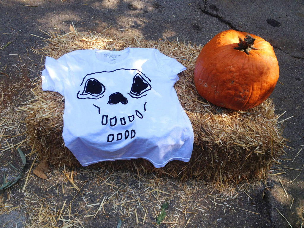 Hand-drawn skeleton on white t-shirt, laying on bale of hay, next to orange pumpkin.