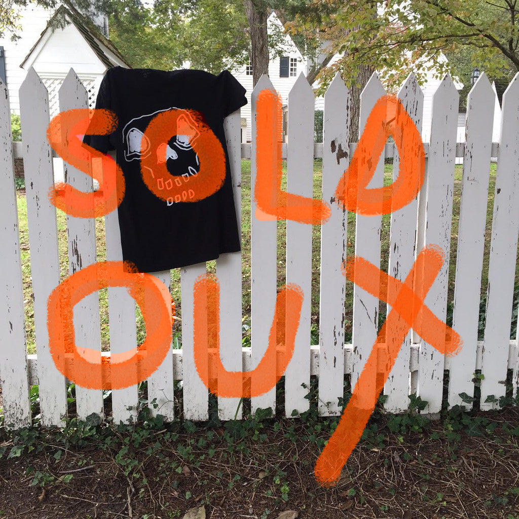Hand-drawn skeleton on black t-shirt hanging on picket fence. Large hand-written text over image that says “Sold Out”.